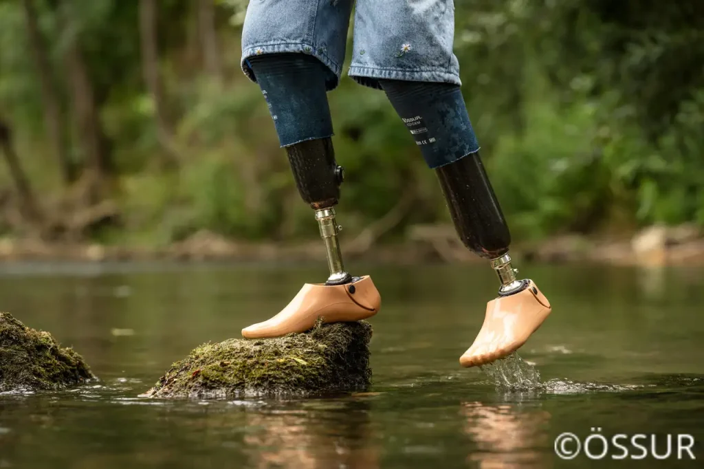 Ein Mann steht mit einer wasserfesten Beinprothese (Badeprothese) sicher auf einem Stein in einem Flusslauf.